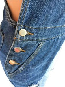 Detail of denim overalls showing contrast stitching, metal buttons, and frayed hemline