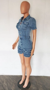 Detail of denim jumpsuit featuring layered fringe tassels and metal button closure