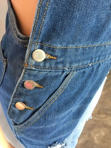 Detail of blue denim overalls showing metal buttons and orange contrast stitching