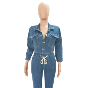Detail of blue denim jumpsuit showing metal buttons, workwear pockets, and white drawstring