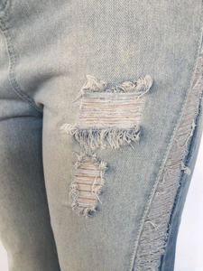 Detail of ripped light blue denim jeans showing frayed white threads and fabric texture
