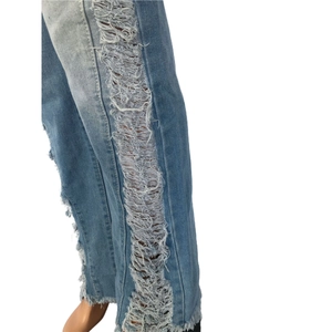 Detail shot of light blue denim pants with vertical tassel fringe and ripped side cutouts