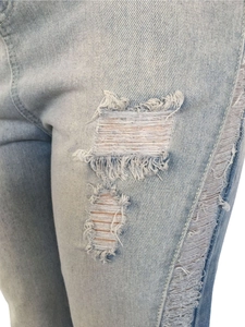 Detailed macro view of distressed light blue denim jeans with ripped holes and frayed edges