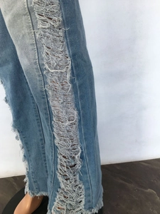 Detailed view of light blue denim jeans featuring frayed edges and side distressed tassels
