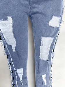 Close-up of light blue distressed jeans with lace-up eyelets and ripped details
