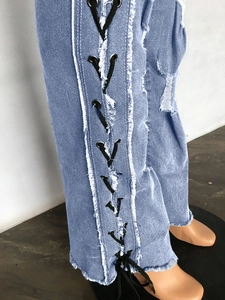 Detail view of light blue denim pants with side lace-up eyelets and frayed hem design