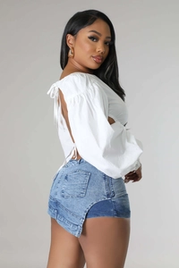 Rear view of white backless lace-up top and asymmetric denim skort on a model