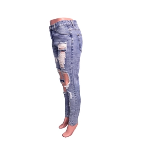 Detail view of distressed blue slim fit denim jeans with ripped holes and washed finish