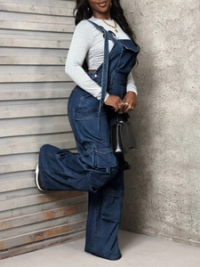 Side view of dark blue denim cargo overalls with large flap pockets and wide leg cut