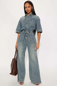 Detail of light blue washed denim jumpsuit with elastic waist and wide-leg flare cut