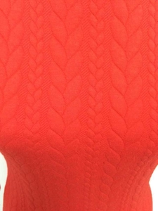 Gros plan d'une robe en tricot rouge montrant la texture des torsades et le tissu élastique