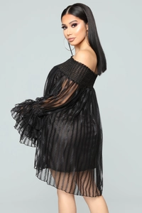 Détail d'une robe noire à épaules dénudées avec poignets à volants et tissu en maille ondulée