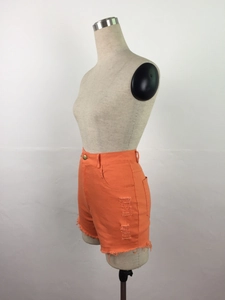Détail du short en jean orange à taille haute avec déchirures latérales et bords effilochés