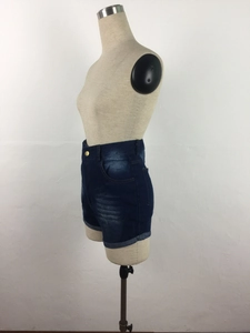 Detail of high waisted dark blue denim shorts with rolled hems and gold button on a mannequin