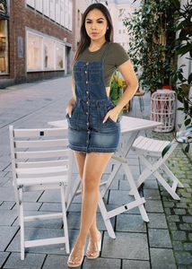 Detail view of denim overall dress with buttons and utility pockets on an outdoor background