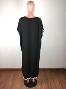 Détail d'un caftan en mousseline noire avec bordures à pompons blancs et coupe ample