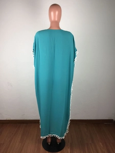 Détail d'un caftan turquoise ample avec bordure à pompons blancs sur le côté et l'ourlet