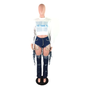 Detail of high waist denim pants featuring sequin panels, ripped holes and long fringes