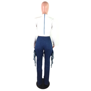 Detail of high-waisted blue jeans featuring distressed side pockets with long fringe tassels
