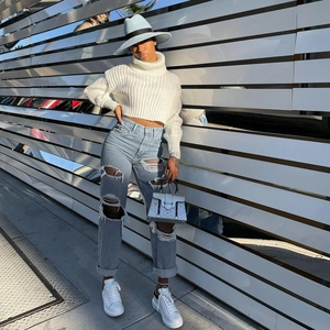 Completo streetwear da donna con maglione corto bianco e jeans azzurri strappati al sole