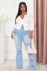 Détail d'un jean évasé bleu clair avec broderies papillon colorées et finitions usées