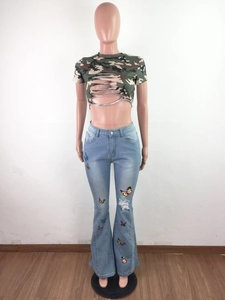Détail du jean évasé taille haute avec broderies papillons colorées et déchirure tendance au genou