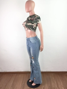 Détail du pantalon en jean évasé avec broderies papillon colorées et genoux déchirés usés