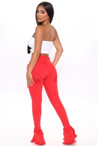 Detail view of red flared denim jeans with distressed holes and ruffled hem design