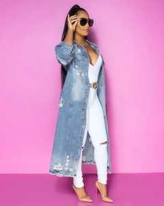 Dettaglio di un trench lungo in denim con strappi e bordi sfrangiati indossato da modella