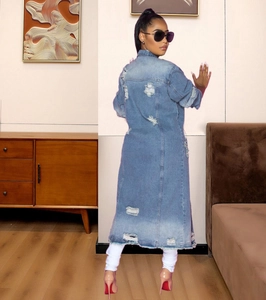 Dettaglio del trench in denim azzurro con fori consumati e taglio lungo alla moda