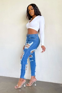 Détail d'un jean bleu slim-fit avec des déchirures usées et une texture brute