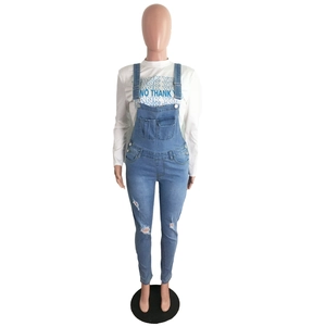 Detail of distressed denim overalls with ripped knees and white long sleeve slogan tee