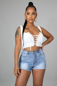 Détail du crop top blanc à lacets avec œillets et short en jean bleu délavé