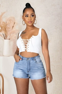 Détail d'un haut court blanc à lacets et d'un short en jean effiloché sur un mannequin