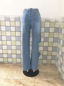 Détail d'un jean droit bleu clair avec une grande déchirure latérale et des poches arrière