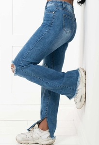 Detail of blue flare jeans featuring distressed knee holes and frayed side split hems