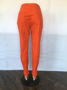 Detail view of bright orange high-waisted stretch denim pants showing back pockets and slim fit