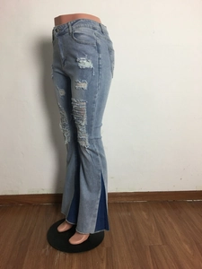 Detail of high waist light blue denim jeans featuring ripped knees and flared patchwork hems