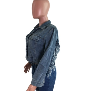 Détail d'une veste courte en jean bleu avec de longues franges sur les manches