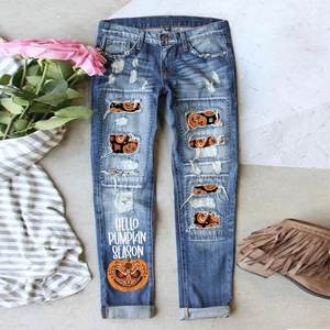 Detail of ripped blue denim jeans featuring Halloween pumpkin prints and festive text