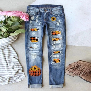 Detail of ripped blue jeans featuring sunflower and pumpkin patchwork and frayed edges