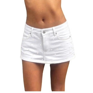Detailed view of white mini denim skirt with elegant pearl embellishments and fringe hem