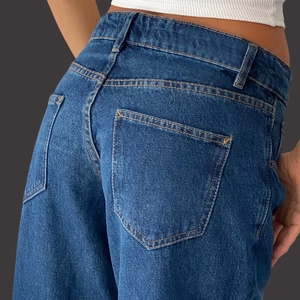 Detail view of high waist dark blue denim jeans showing contrast yellow stitching and pockets