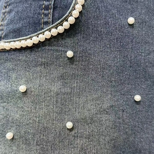 Detail of dark blue denim fabric featuring white pearl embellishments and yellow stitching