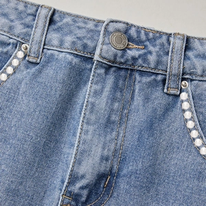 Detail of light blue denim shorts featuring pearl embellishments on the pocket edge