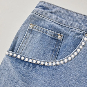 Detailed close-up of light blue denim fabric featuring elegant white pearl bead trim