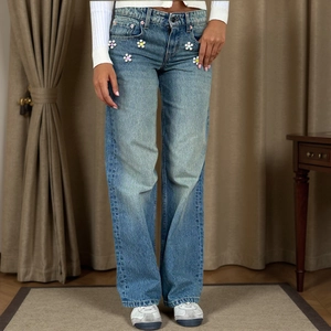 Detail of light blue wide-leg jeans featuring white floral appliqués on the pockets