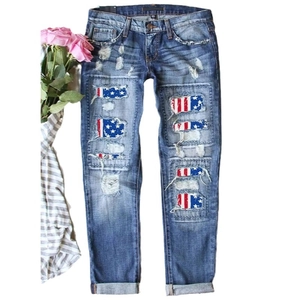 Distressed blue denim jeans featuring ripped details and American flag fabric inserts