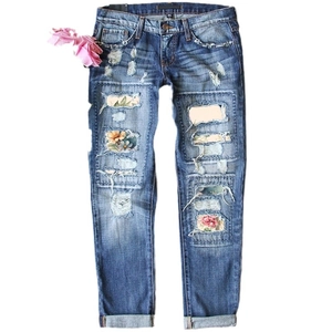 Women's distressed blue denim jeans with floral patch embroidery and pink flower accessory