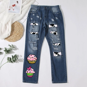 Detail of distressed dark blue jeans with cow print patches and cupcake graphics
